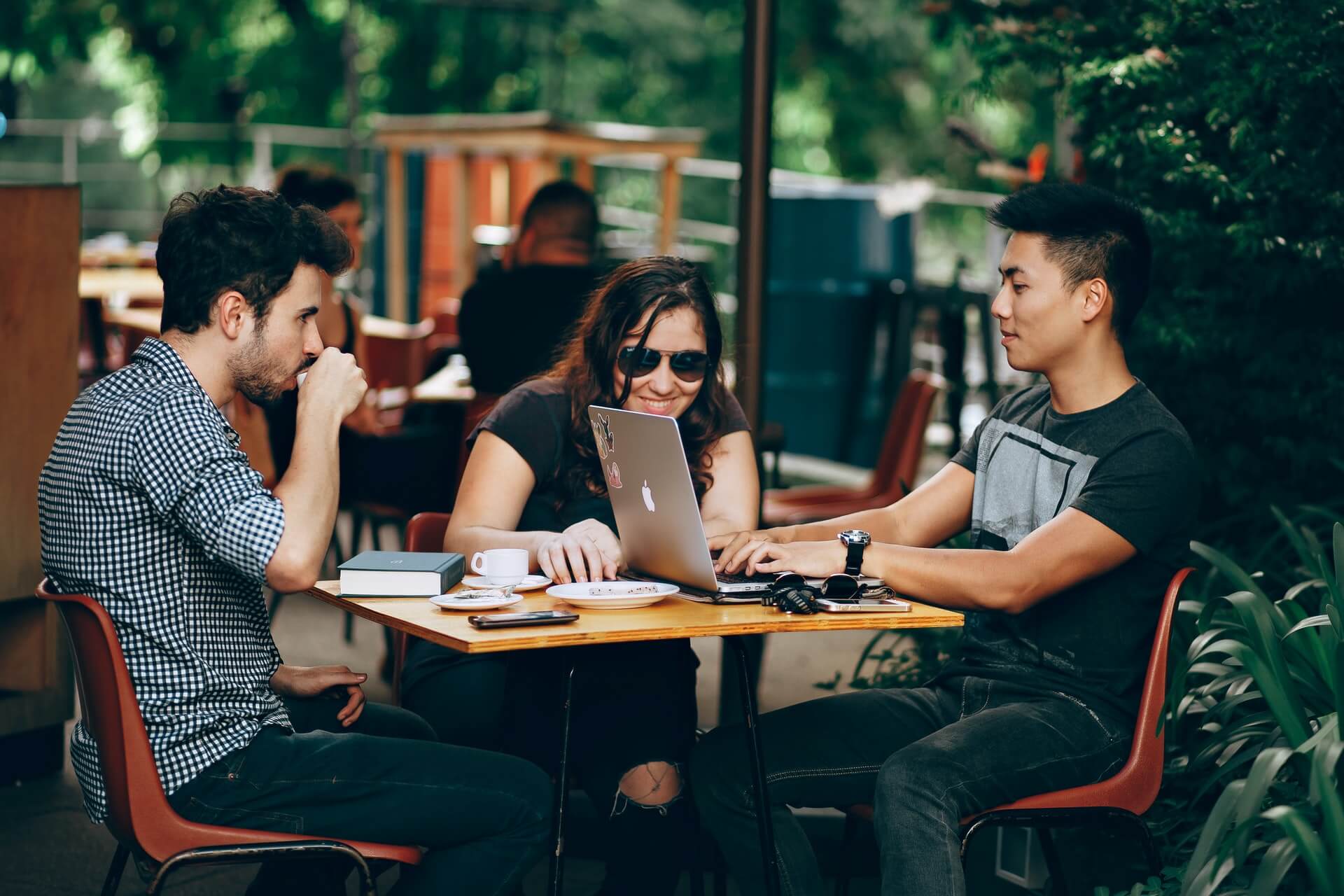 Tres jóvenes trabajando en una cafetería usando una computadora portátil.